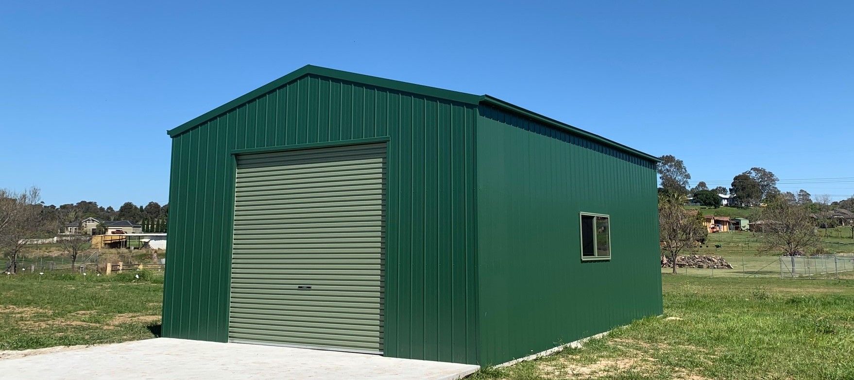 A Green Shed With a Roll Up Door and a Window — ShedPro Constructions in Mid North Coast, NSW