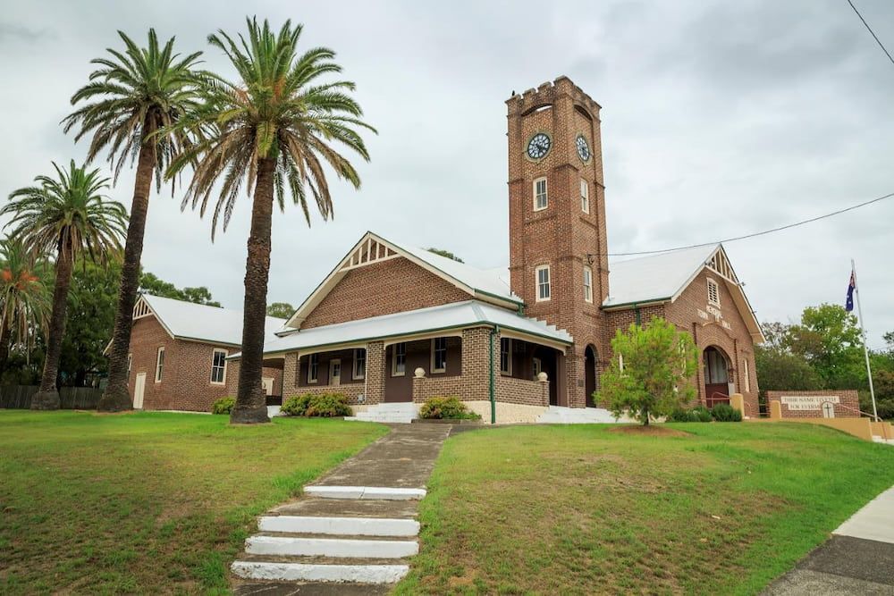 A Brick Building With a Clock Tower and Palm Trees — ShedPro Constructions in Wingham, NSW