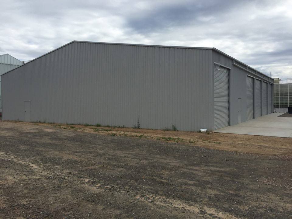 A Large Gray Building Is Sitting in The Middle of A Dirt Field — ShedPro Constructions in Darawank, NSW