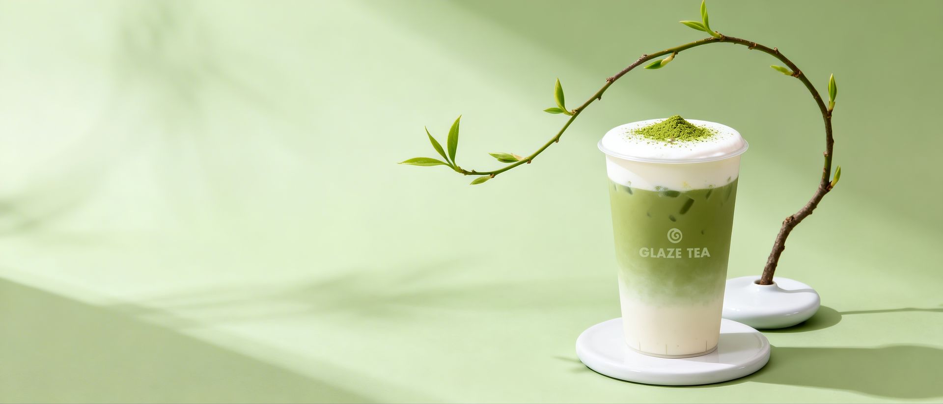 A white takeaway cup labeled "GLAZE TEA" suspended in the air, encircled by two white calla lily flowers against teal.