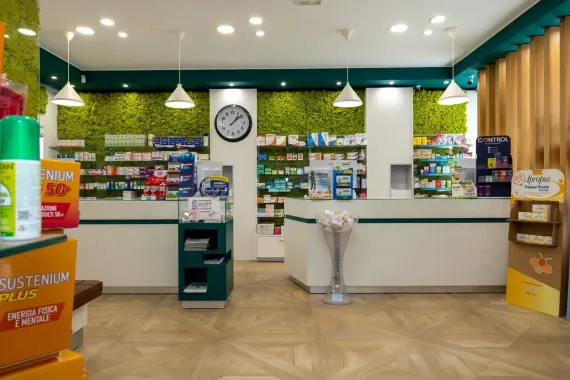 Una persona in camice bianco utilizza un tablet nel corridoio di una farmacia.