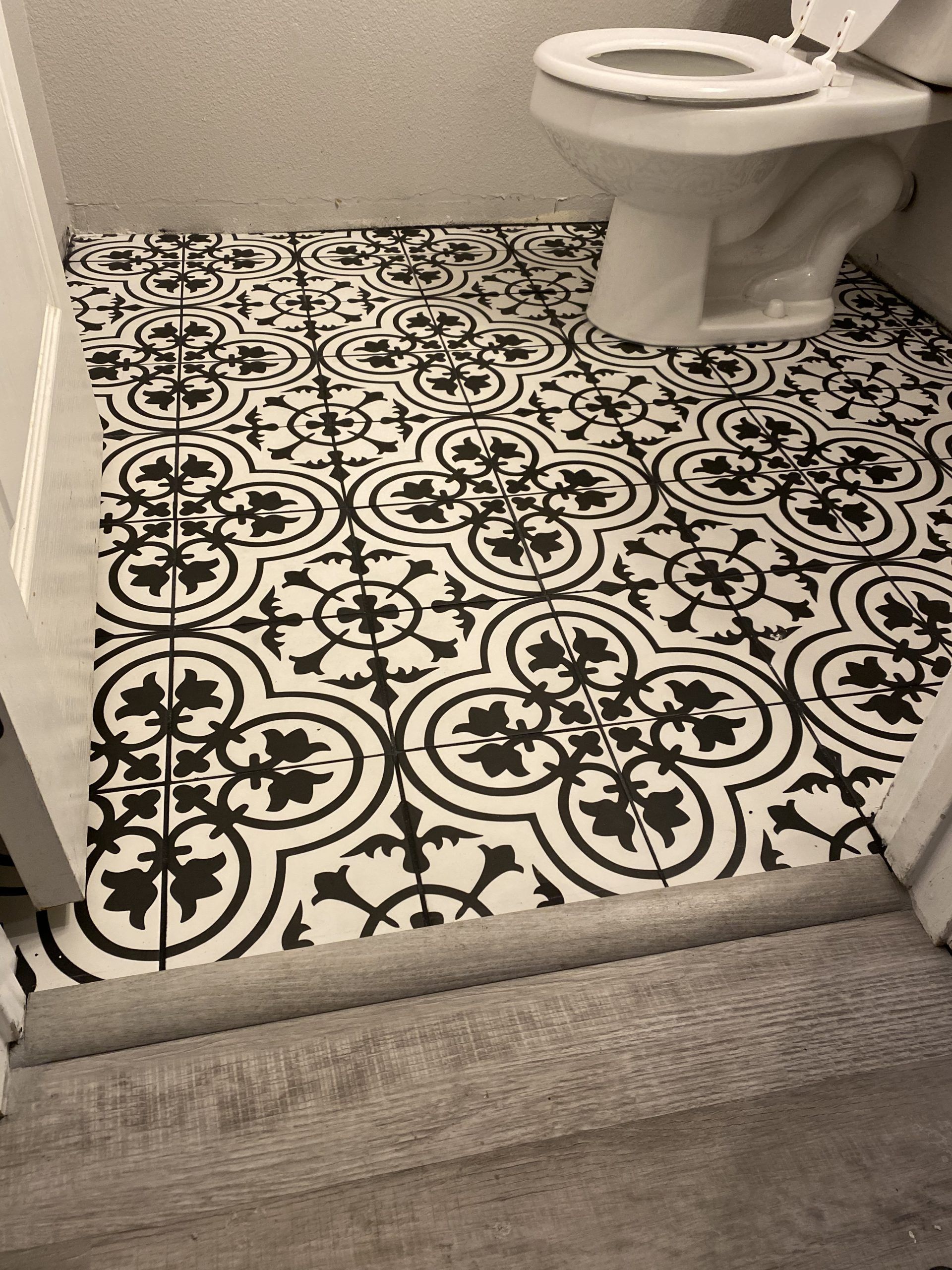 Bathroom with black-and-white patterned tile floor and a white toilet near a carpeted threshold