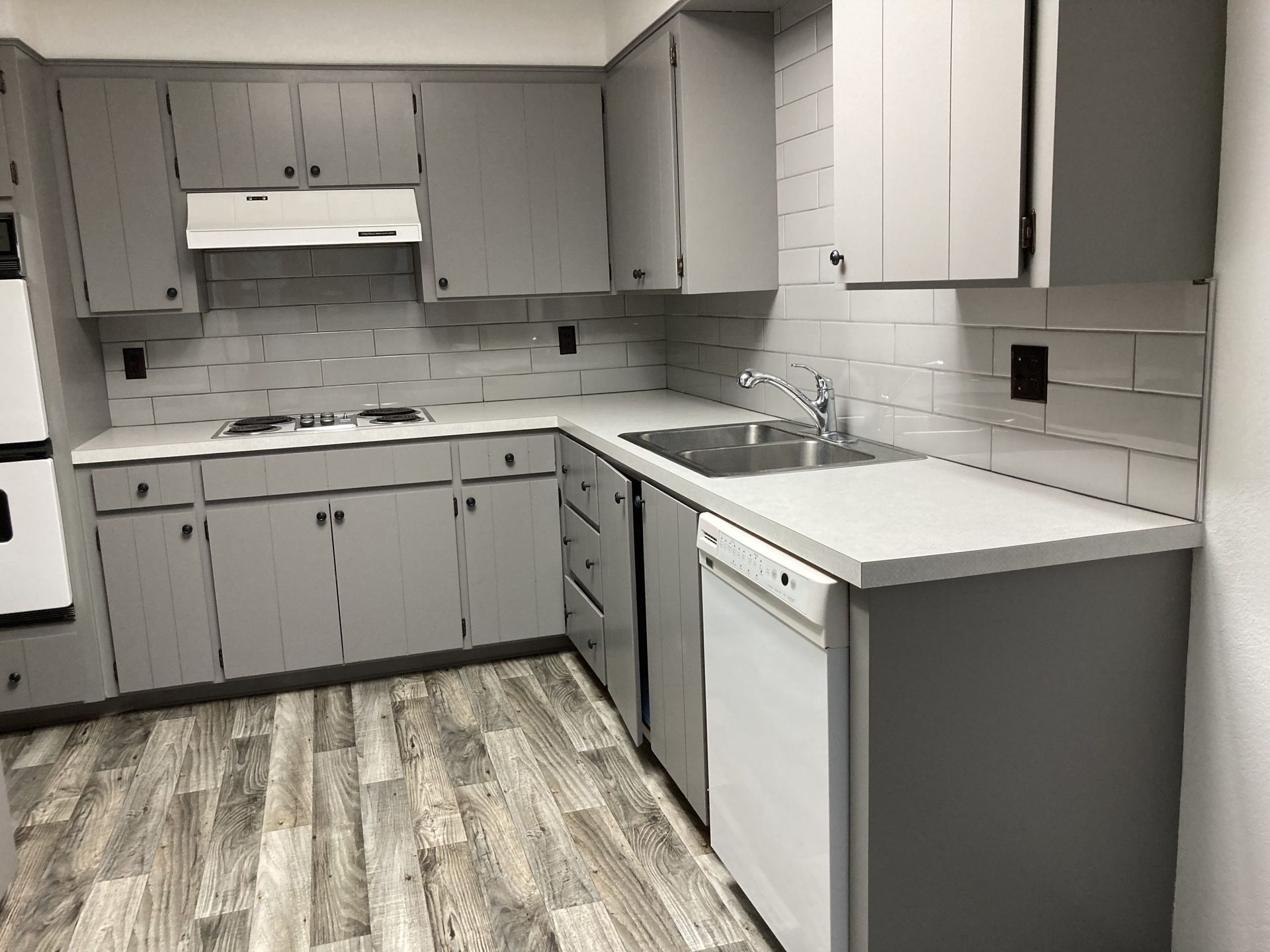 Small modern kitchen with gray cabinets, white countertops, tile backsplash, and wood-look flooring