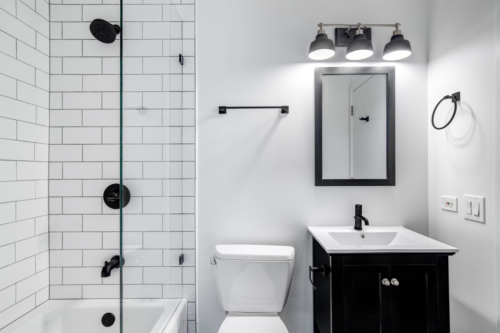 Modern white bathroom with shower, toilet, vanity sink, mirror, and black fixtures
