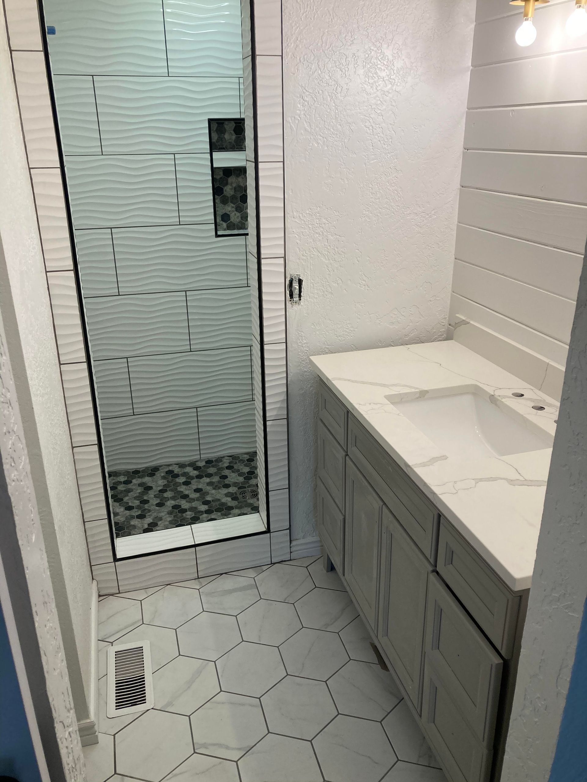 Narrow white-tiled bathroom with vanity, sink, and glass shower door with frosted paneling