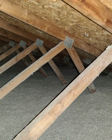 Inside of an attic with wooden rafters and insulation on the floor.