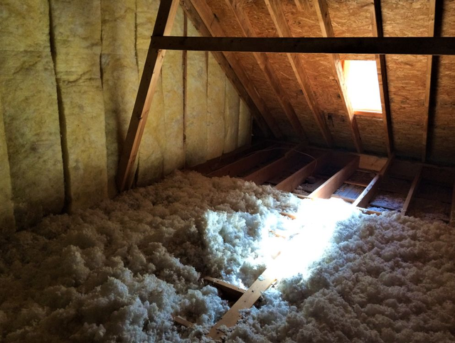 Attic with exposed beams and insulation, sunlight streaming through a roof window