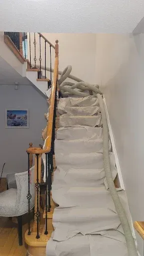 A staircase with beige protective floor covering draped over the steps, featuring a flexible hose running up the center.