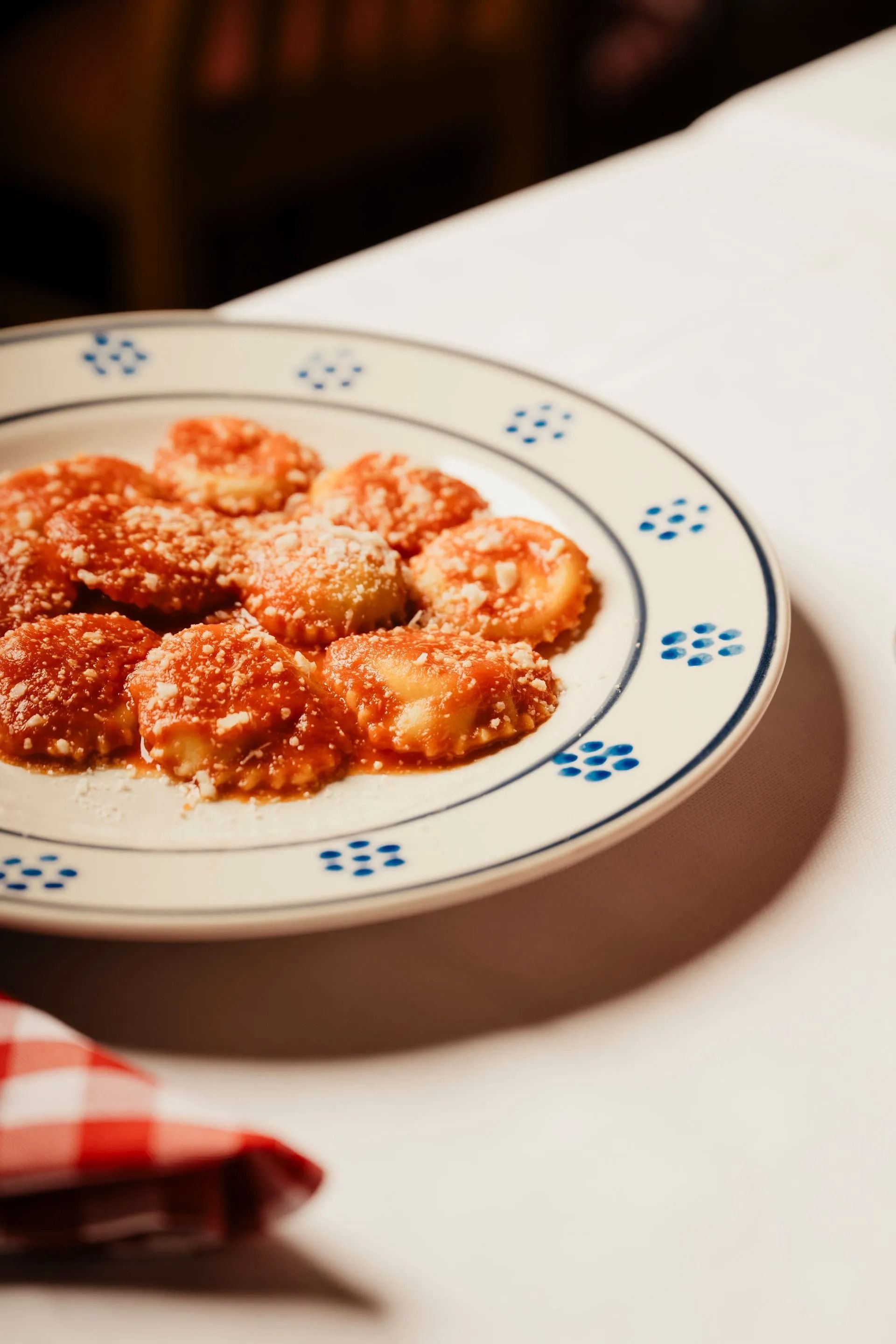 Un piatto di ravioli al sugo di pomodoro su un tavolo bianco, con un tovagliolo a quadretti rossi accanto.