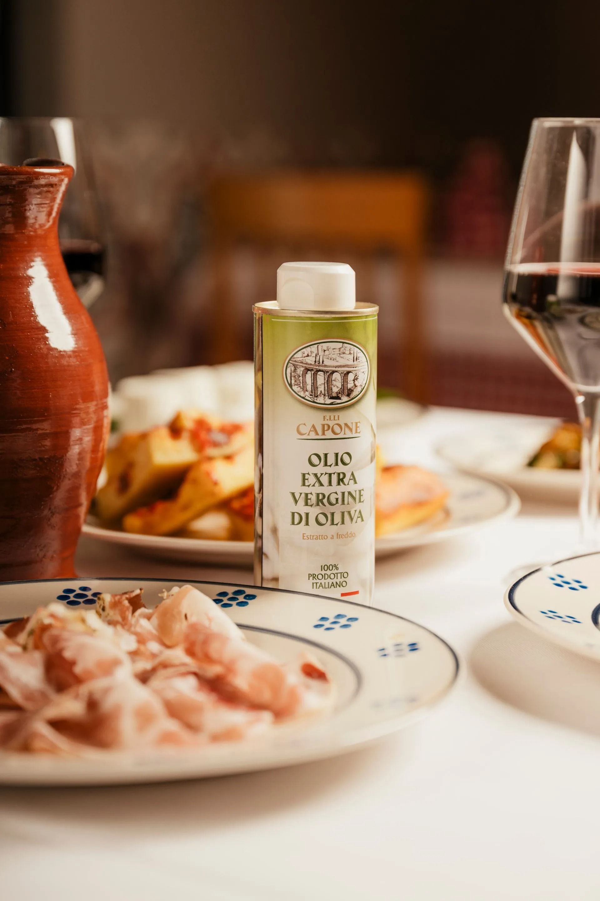 Tavolo da ristorante con piatti di pasta, bottiglia di olio d'oliva, pane e un bicchiere di vino rosso.