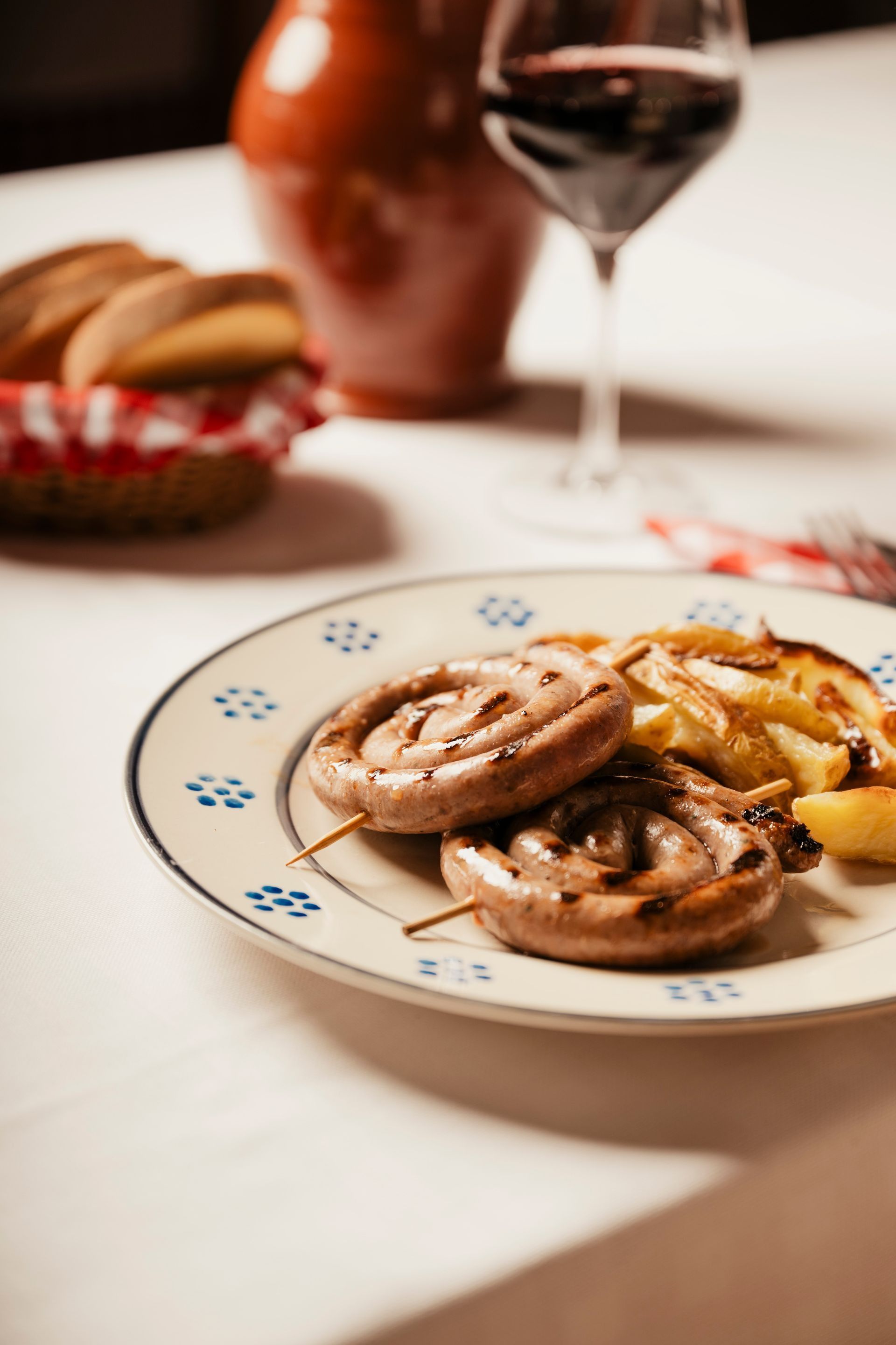 Un piatto con funghi e patate grigliate su un tavolo, con un bicchiere di vino e del pane sullo sfondo.