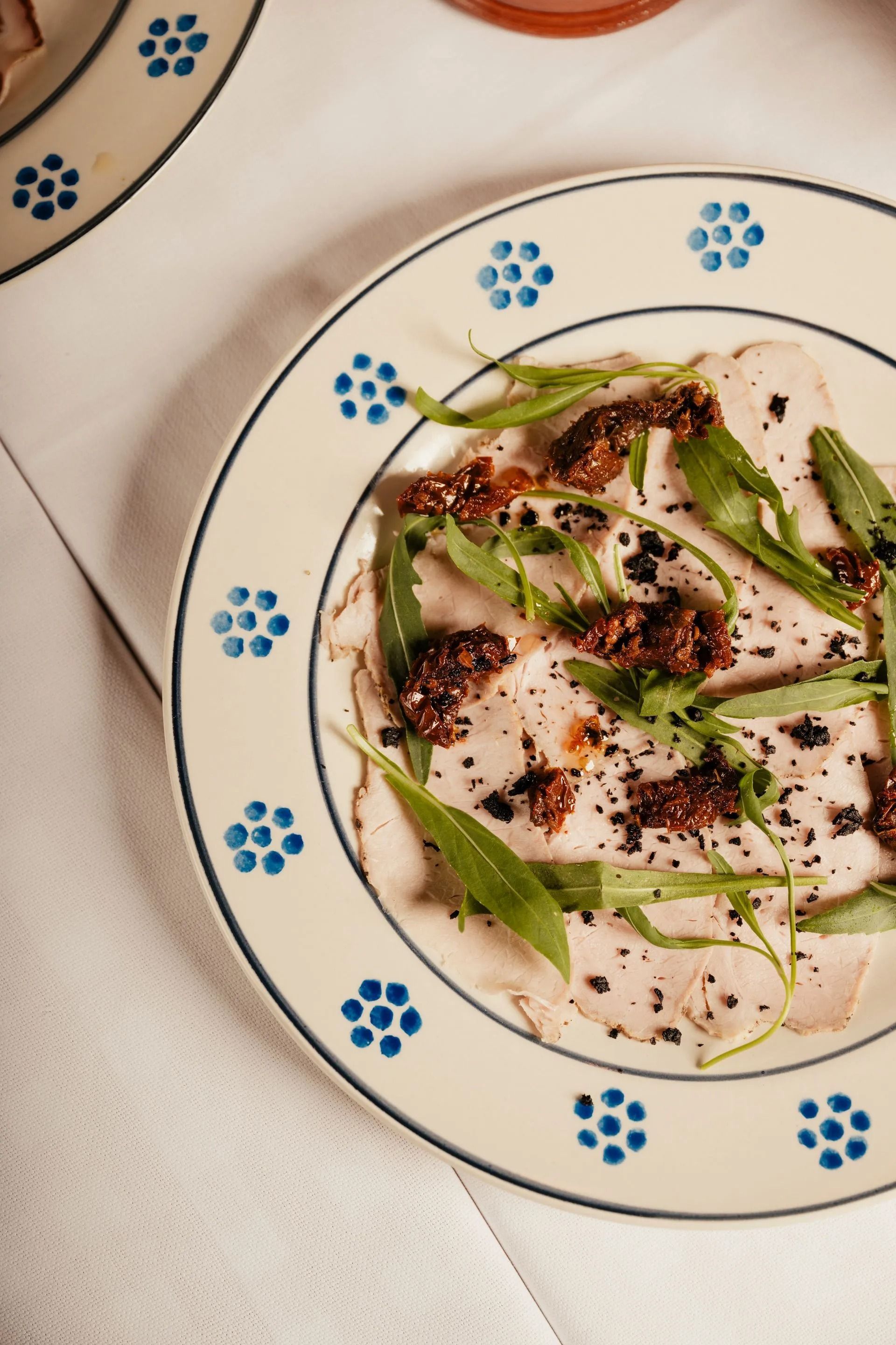 Pesce arrosto con erbe aromatiche e salsa, servito su un piatto bianco con bordo floreale blu.