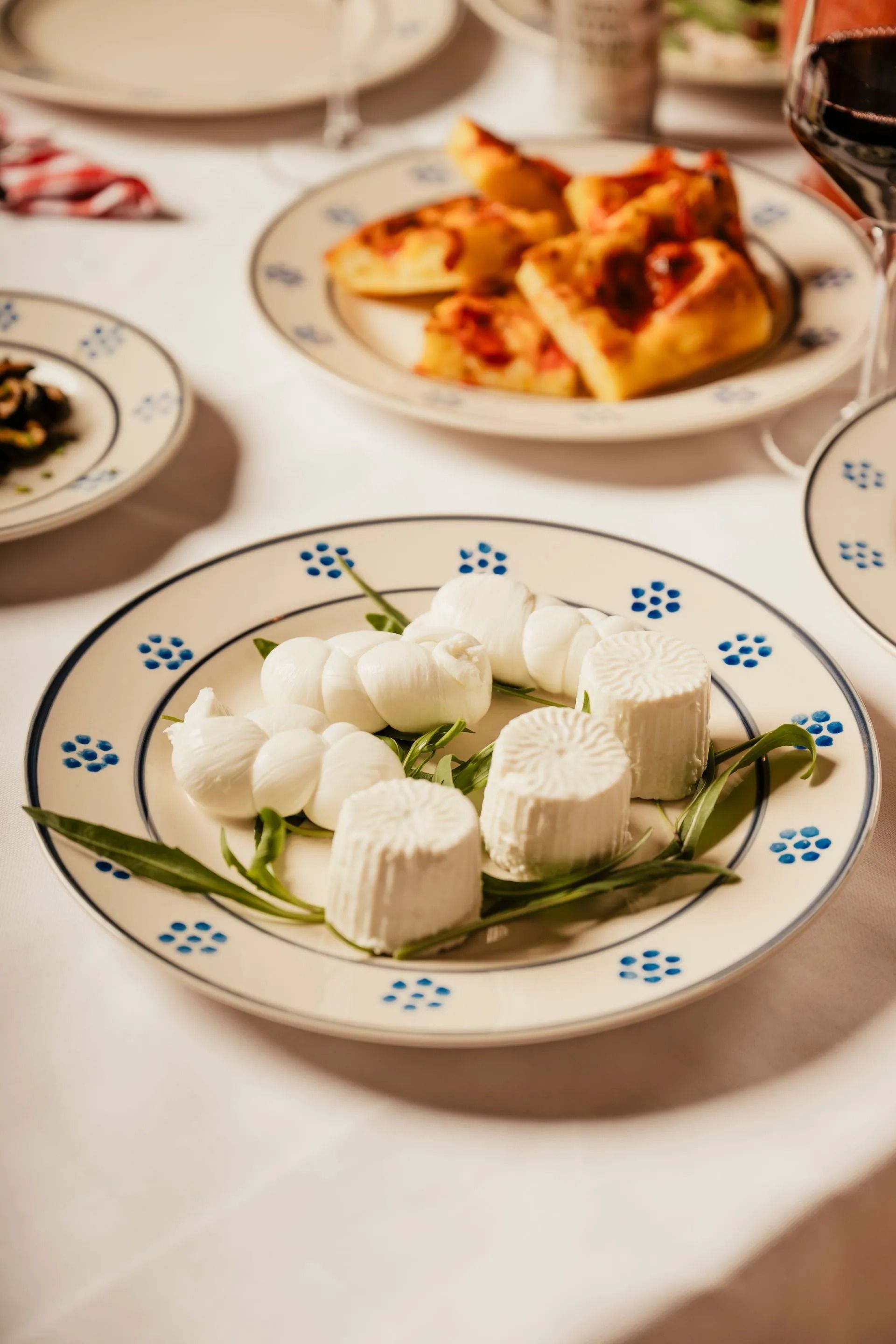 Formaggio bianco a fette e fiori su un piatto decorativo su un tavolo da pranzo, con la pasta sullo sfondo.