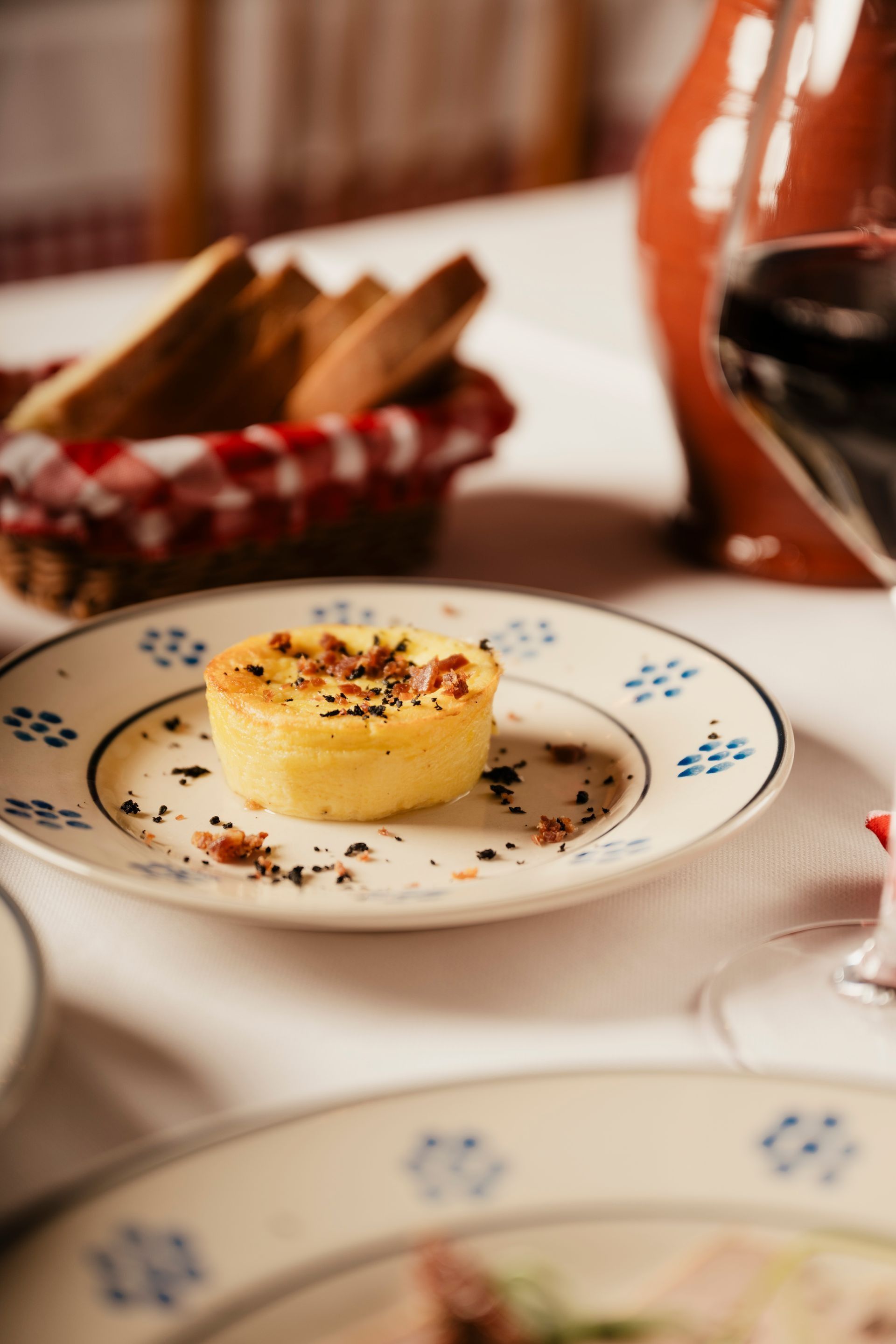 Torta dolce su un piatto floreale con briciole di cacao, accanto a un bicchiere di vino rosso su un tavolo