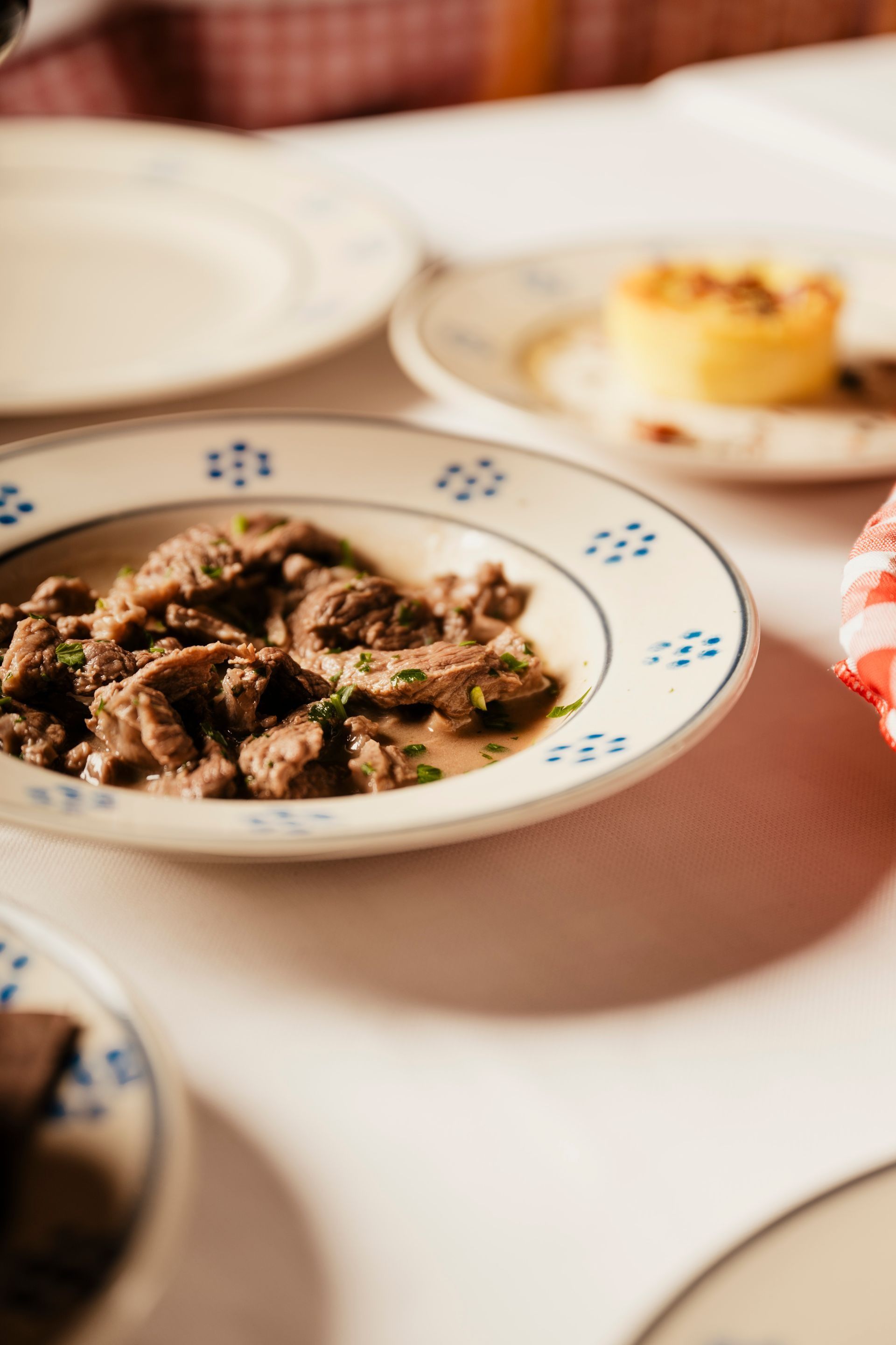 Piatti di spezzatino di manzo e dessert su un tavolo con tovaglia bianca e piatti decorati.