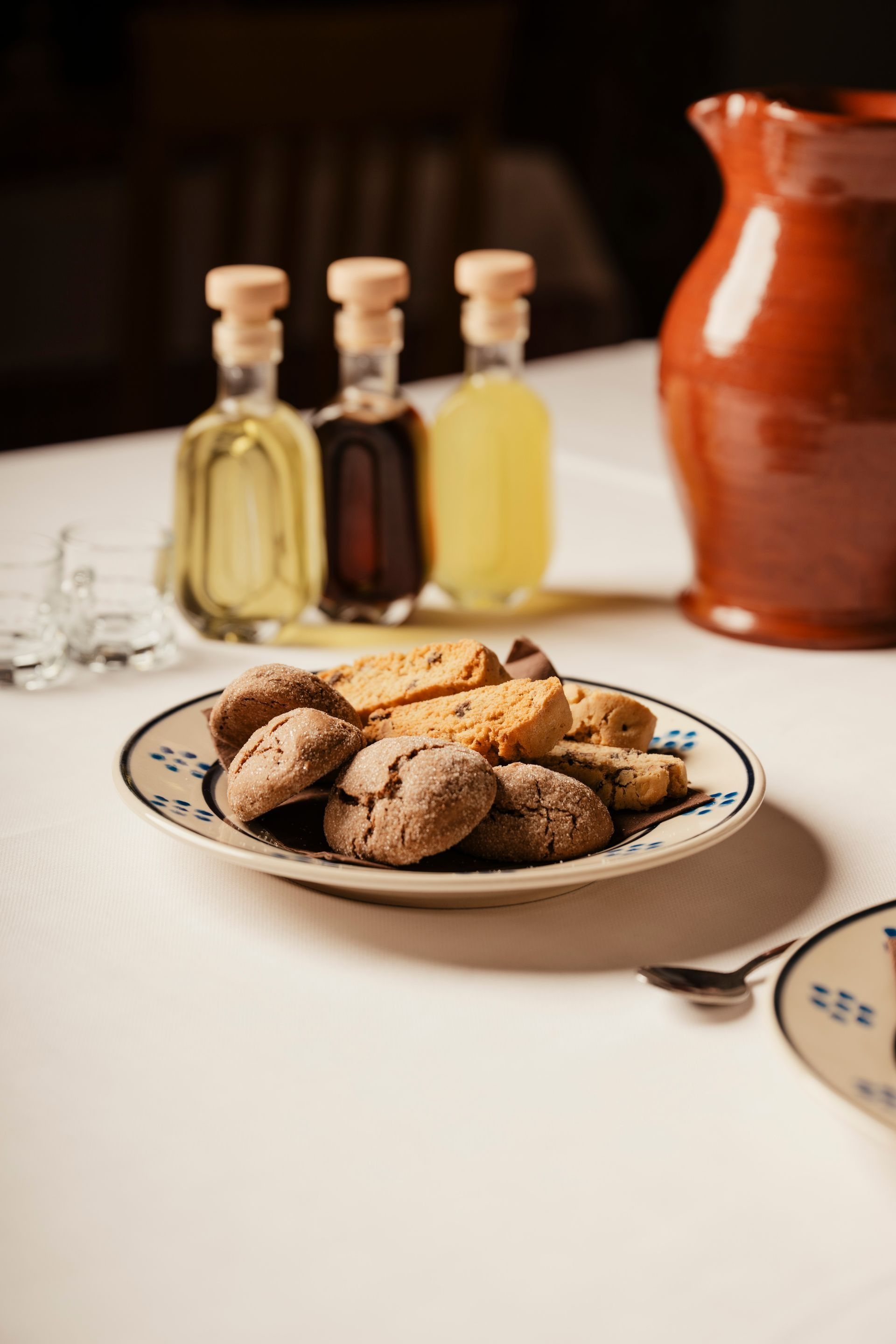 Un piatto di biscotti su un tavolo con delle bottigliette e una brocca di terracotta sullo sfondo.