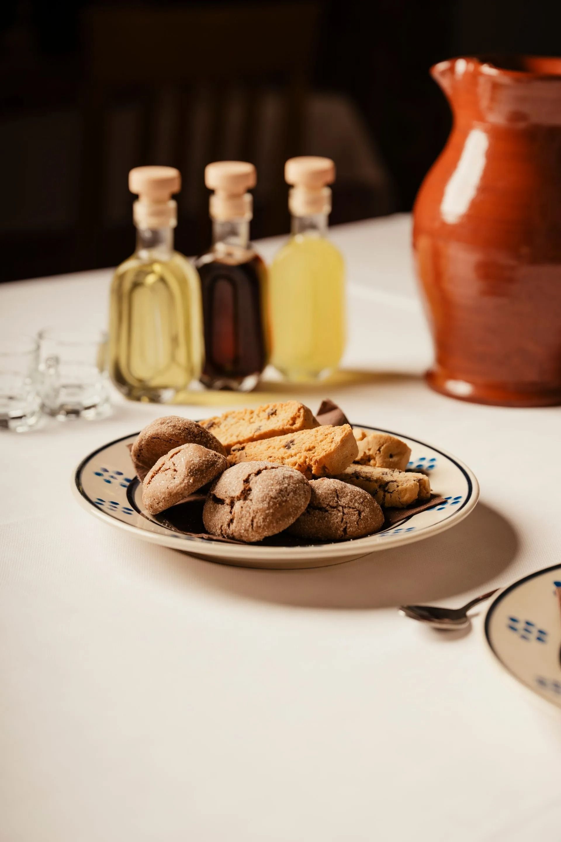 Un piatto di biscotti su un tavolo con delle bottigliette e una brocca di ceramica rossa sullo sfondo.