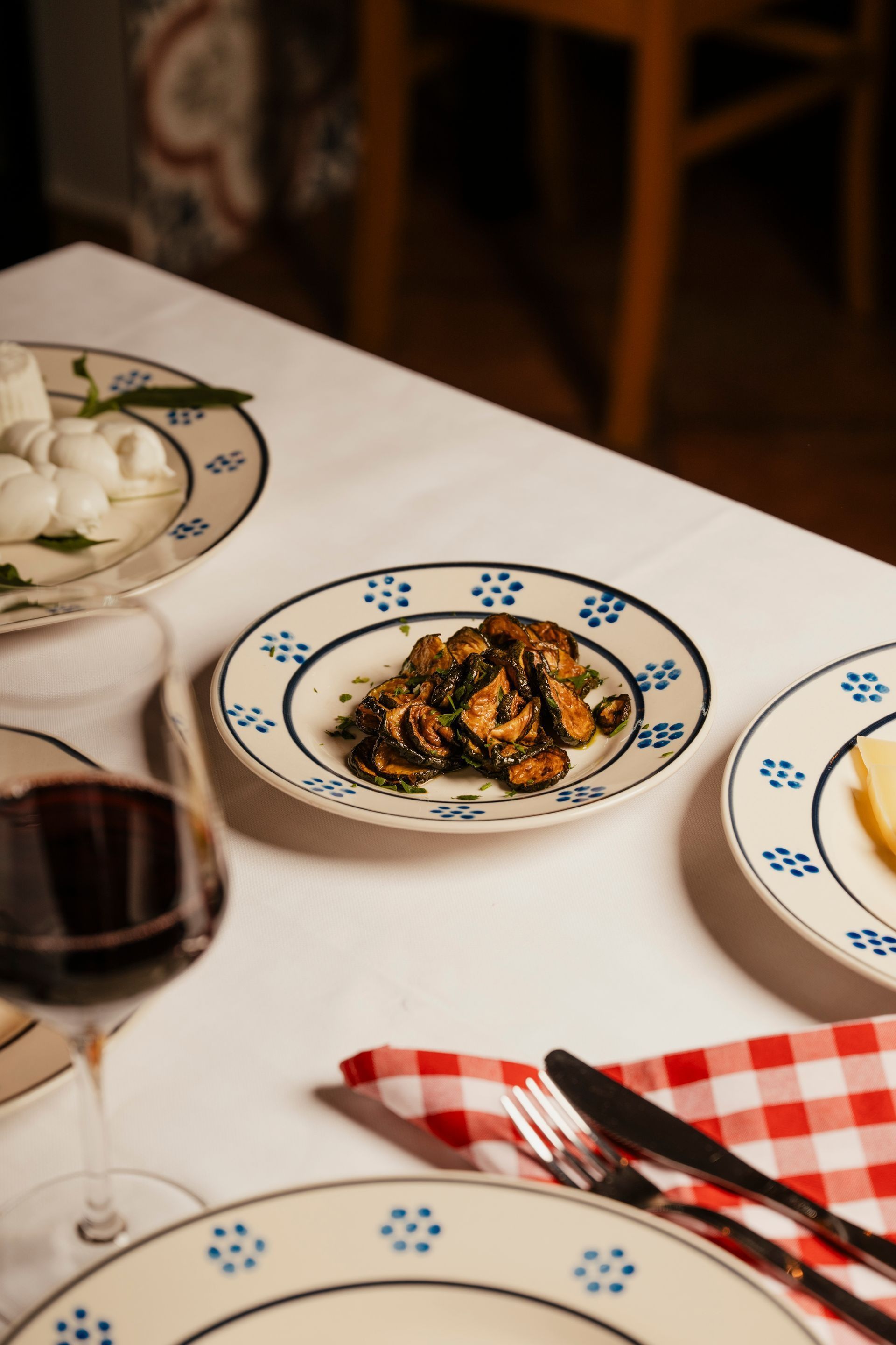 Apparecchia la tavola con piatti decorati, un bicchiere di vino rosso e un tovagliolo a quadri rossi accanto a un piatto di cibo.