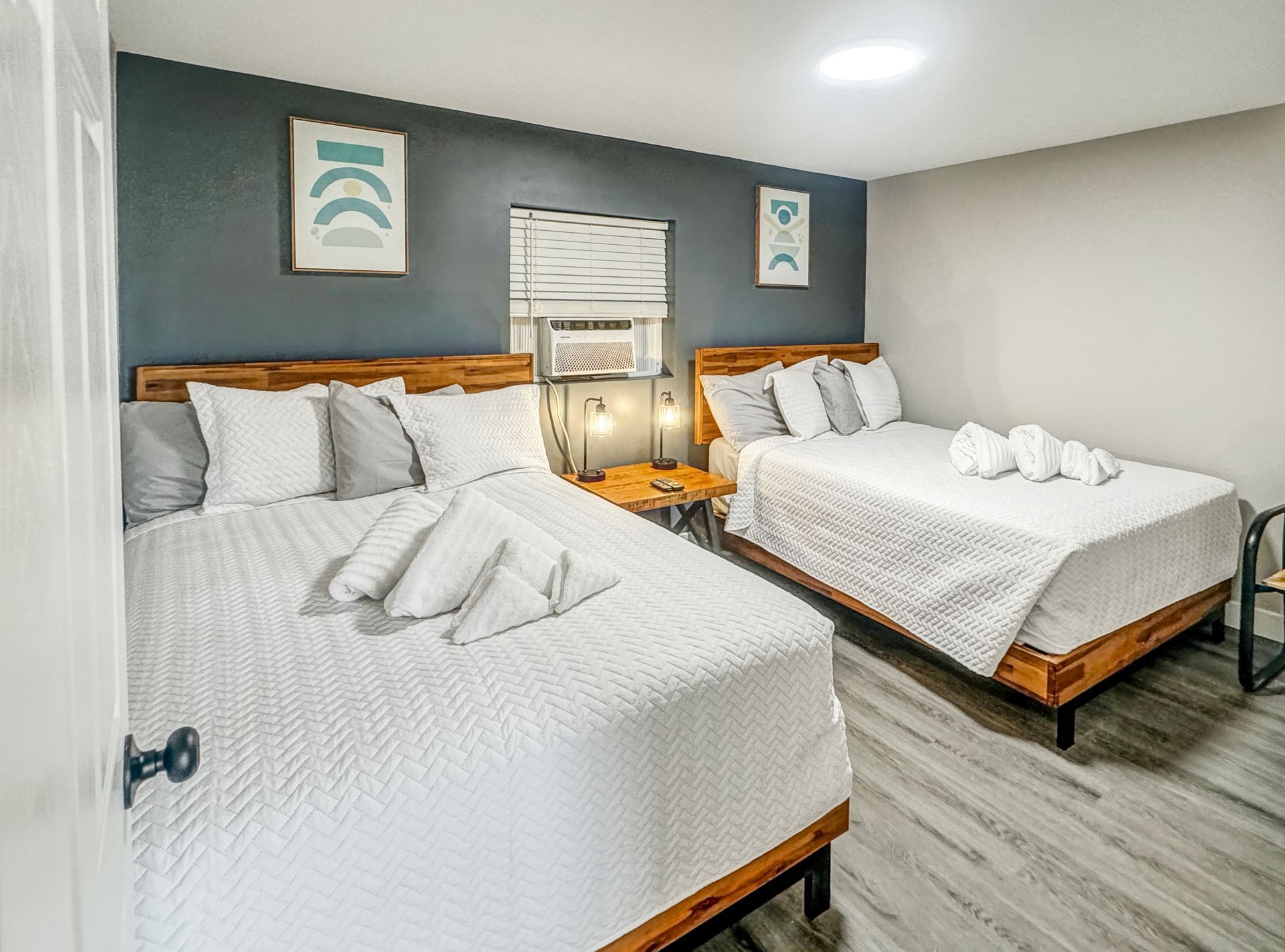 A bedroom with two beds, one queen-sized and one full-sized. The beds have white bedding. The walls are blue and gray.