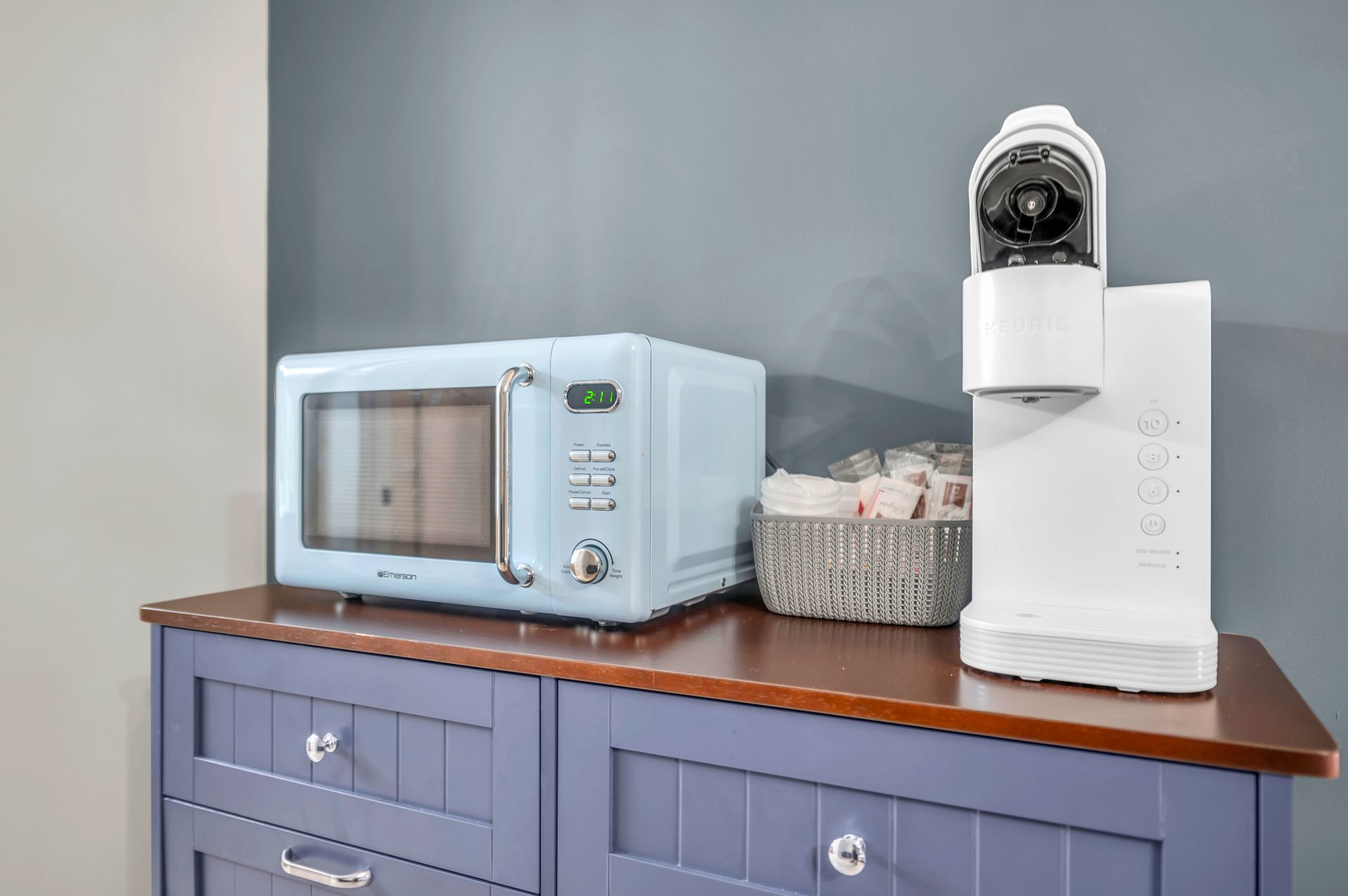 Blue microwave and coffee maker on a blue cabinet against a gray wall.