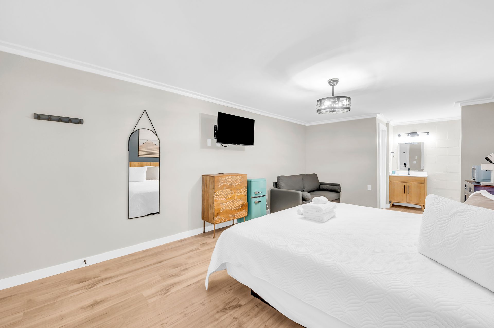 Bedroom with white bed, TV, dresser, mirror, and a small sofa.