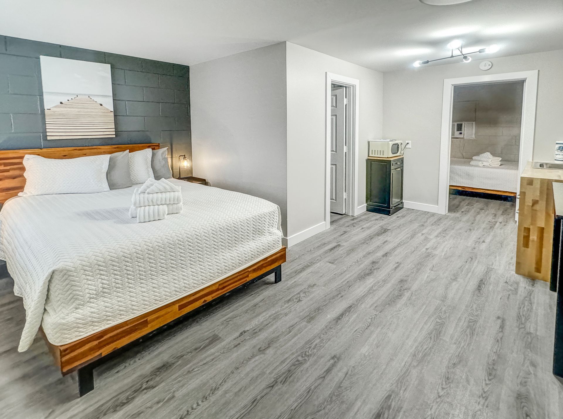A studio apartment with a bed, bathroom, and kitchenette. Gray walls and wooden bed frame.