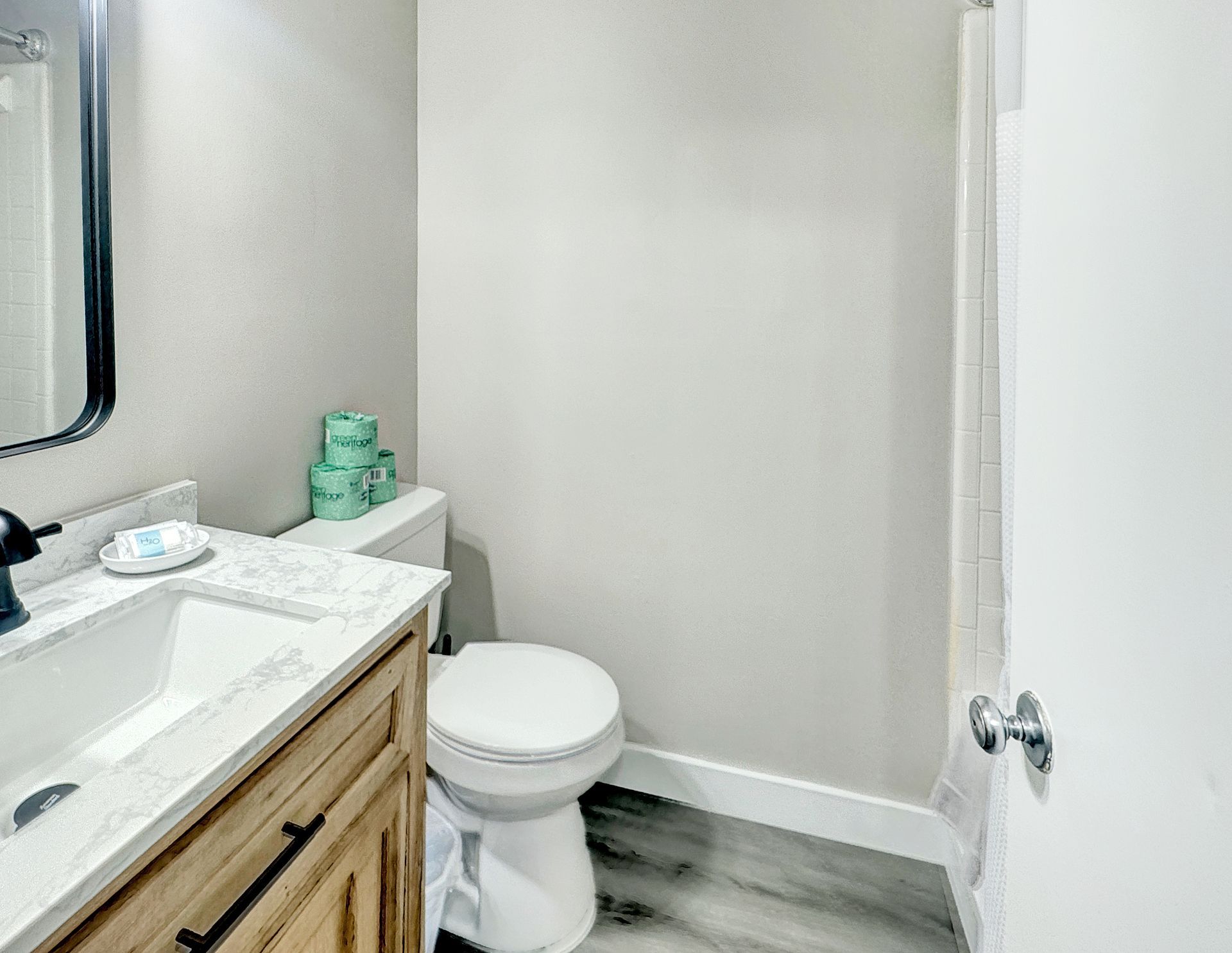 Small bathroom with a white toilet, sink, and wood-tone vanity. Light gray walls and floor.