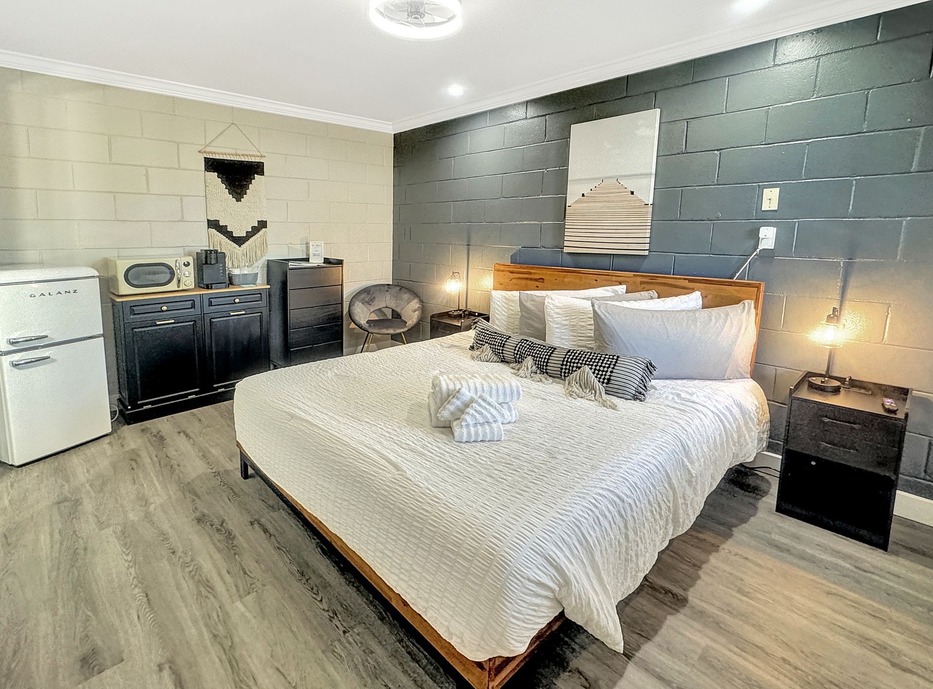 Bedroom with a wooden bed, a white comforter, dark accent wall, and retro refrigerator. Gray and white color scheme.