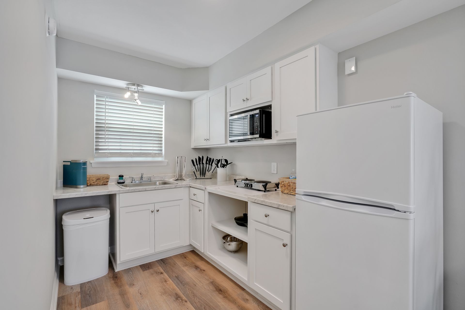 Small, white kitchen with appliances, cabinets, and a window.