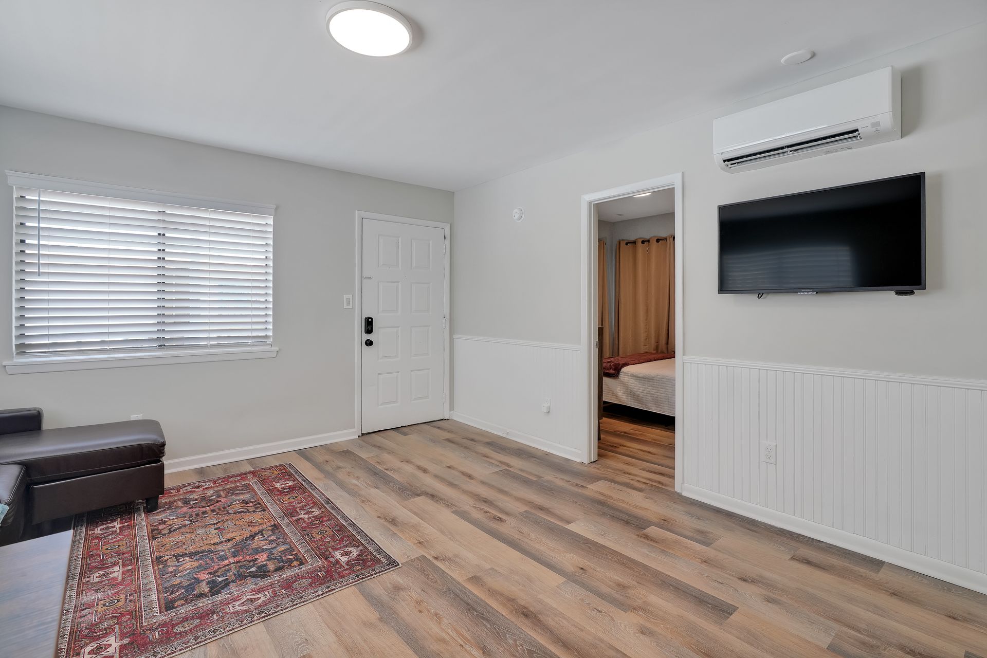 Living room with light wood floors, a rug, TV, and open doorway to a bedroom.