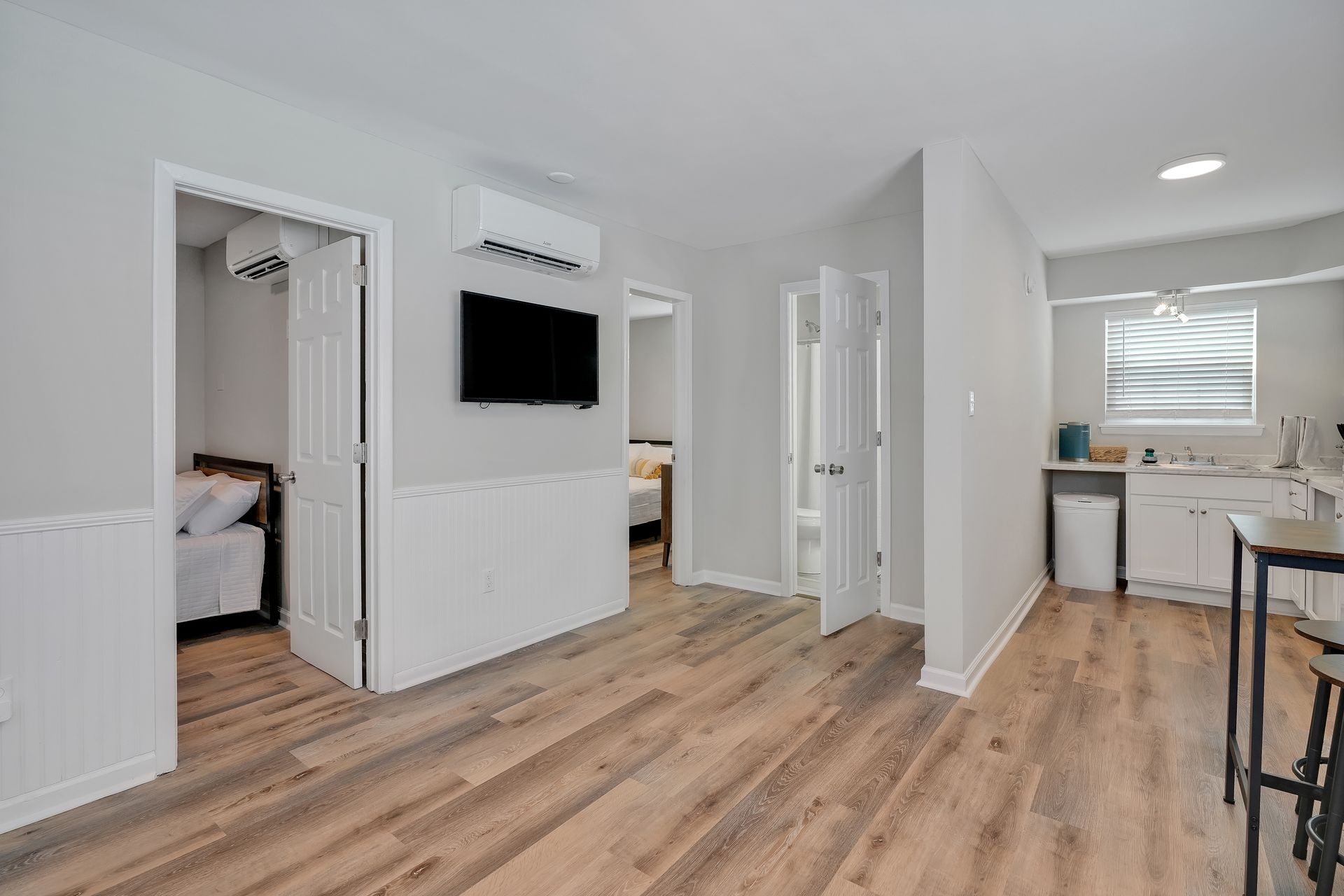 Interior view of a small apartment with light wood floors, white walls, and a small kitchen visible.
