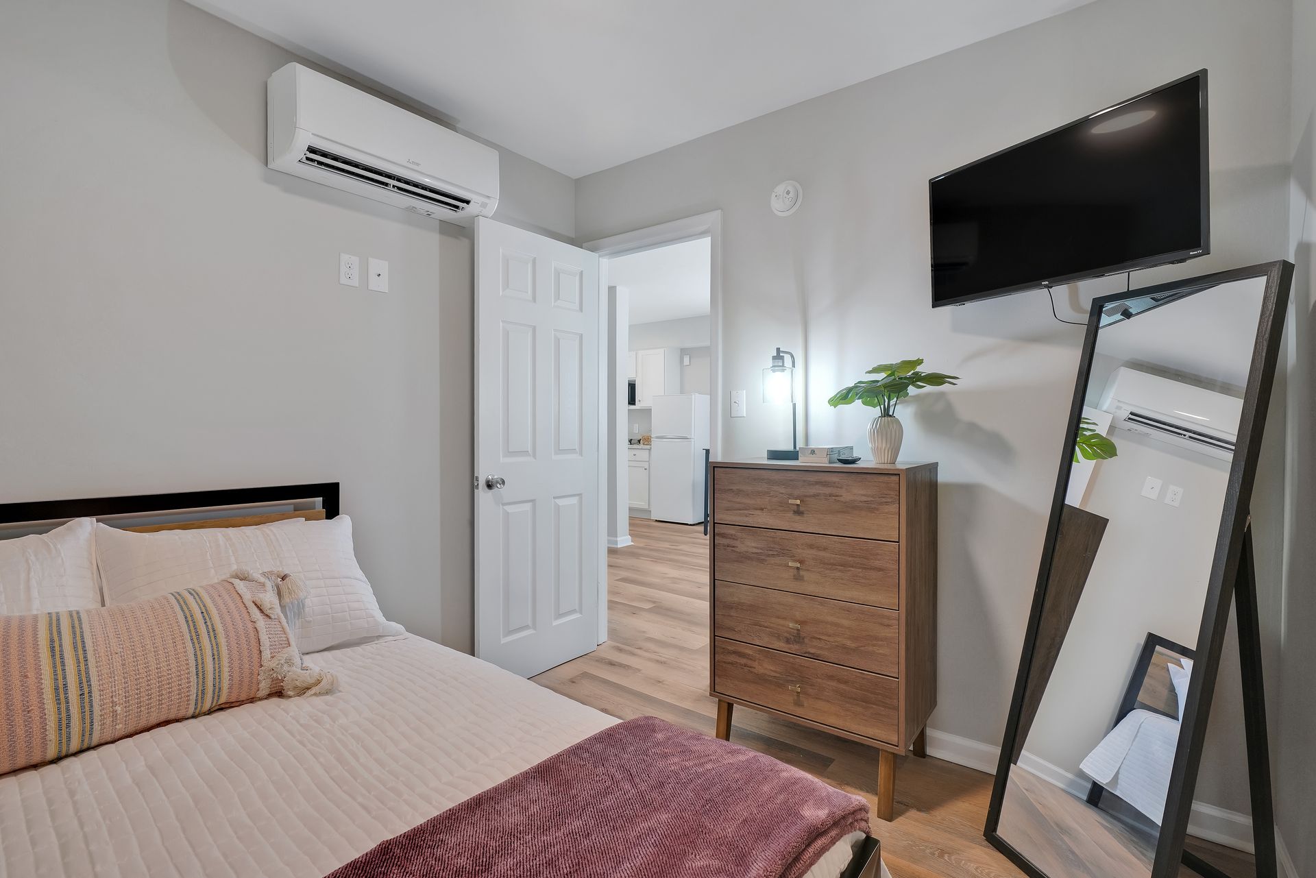 Bedroom with bed, dresser, mirror, TV, and open door to kitchen.