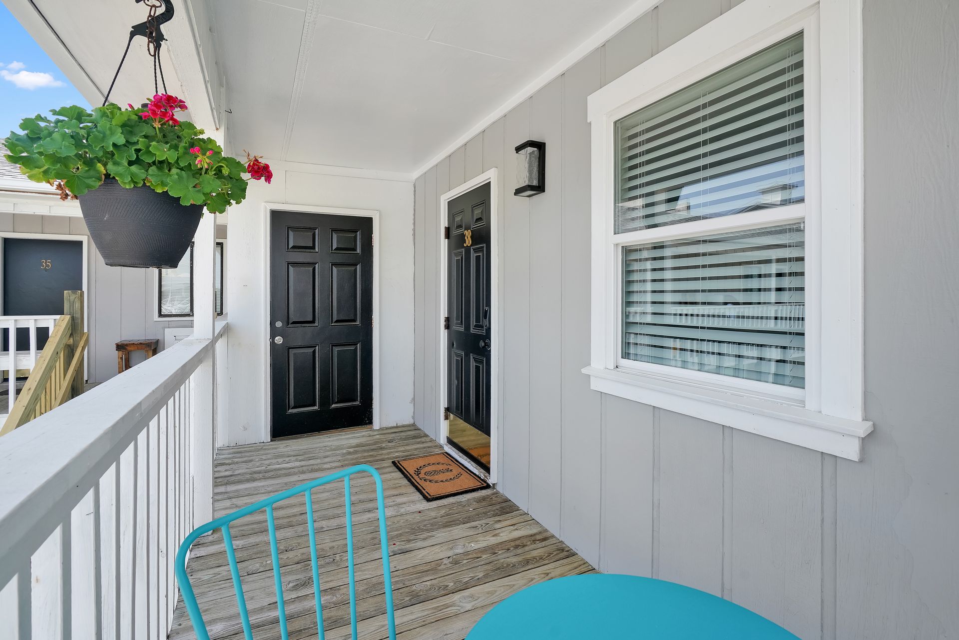 A small porch with two black doors, a window, blue chair, and hanging flower pot.