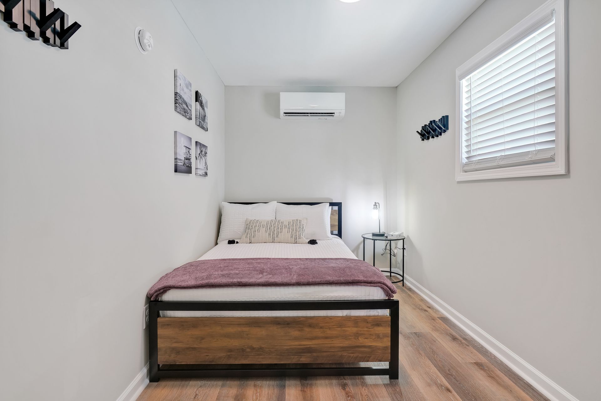 Small bedroom with a bed, window, and air conditioner. Walls are gray, floor is wood-like.