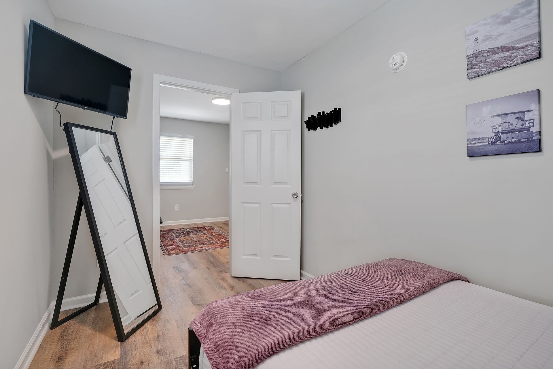 Bedroom with bed, mirror, TV, door to another room, gray walls, and wood-look flooring.