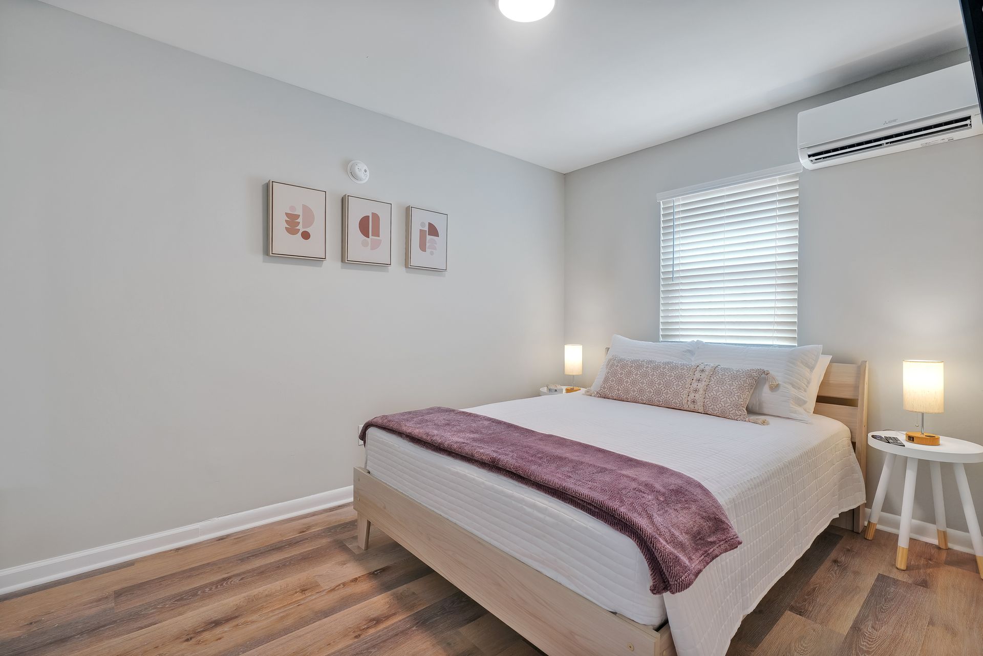 Bedroom with a bed, small side table, artwork, and window with blinds.