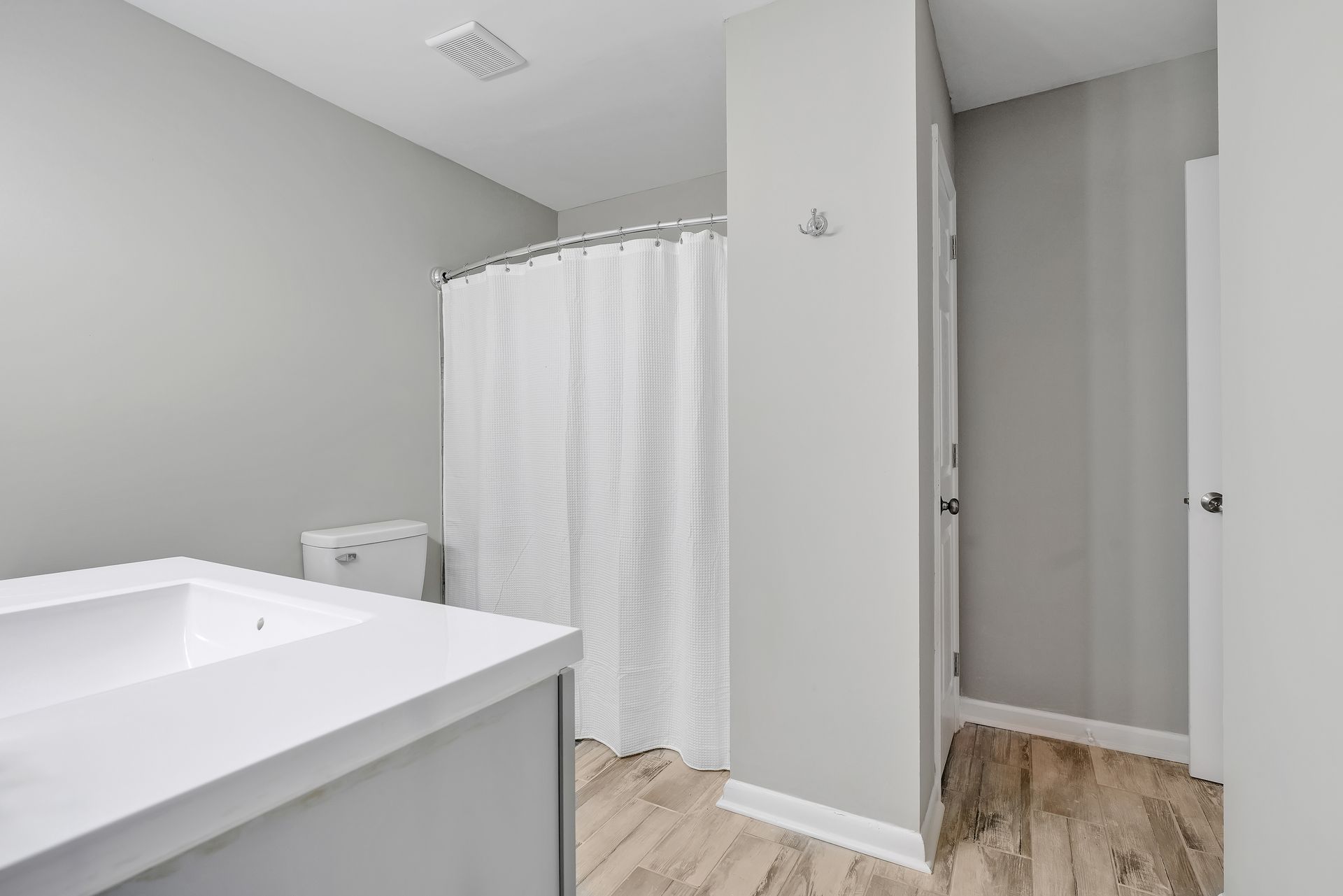 Bathroom with white sink and shower curtain, grey walls, and light wood-look flooring.