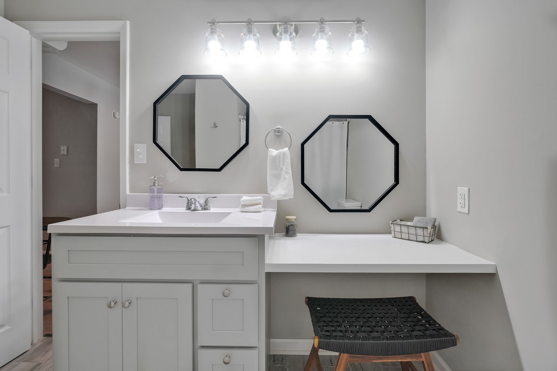 Bathroom vanity with two octagon mirrors, a white countertop, and a black stool.