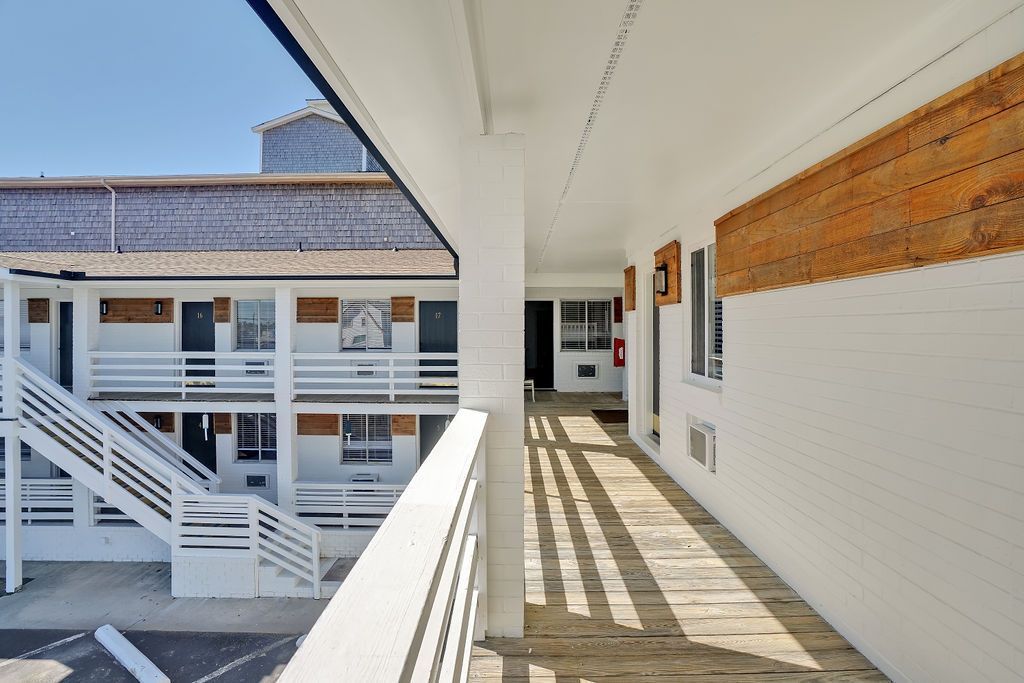 Exterior view of a motel hallway with a wooden walkway. White railings and walls. Building has a wooden roof.