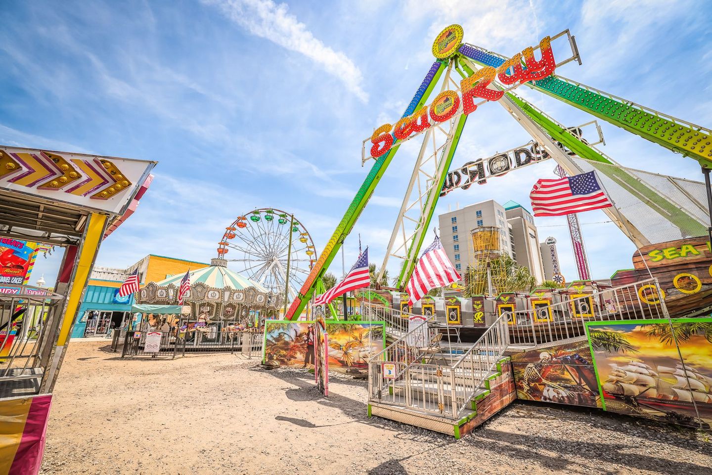 Amusement park scene with a large pirate ship ride, Ferris wheel, and American flags against a blue sky.