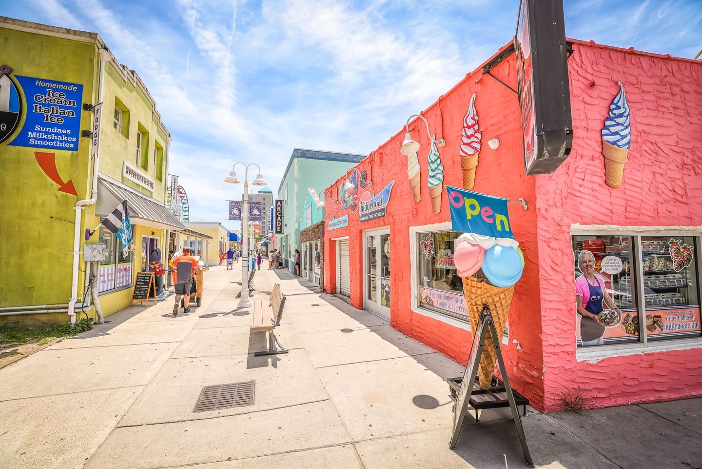 A colorful street lined with shops, including an ice cream parlor with a large cone sign and open sign, under a blue sky.