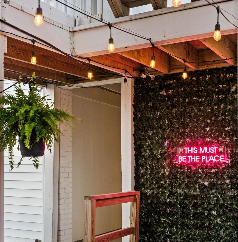 Outdoor patio with string lights, hanging fern, and neon sign reading 