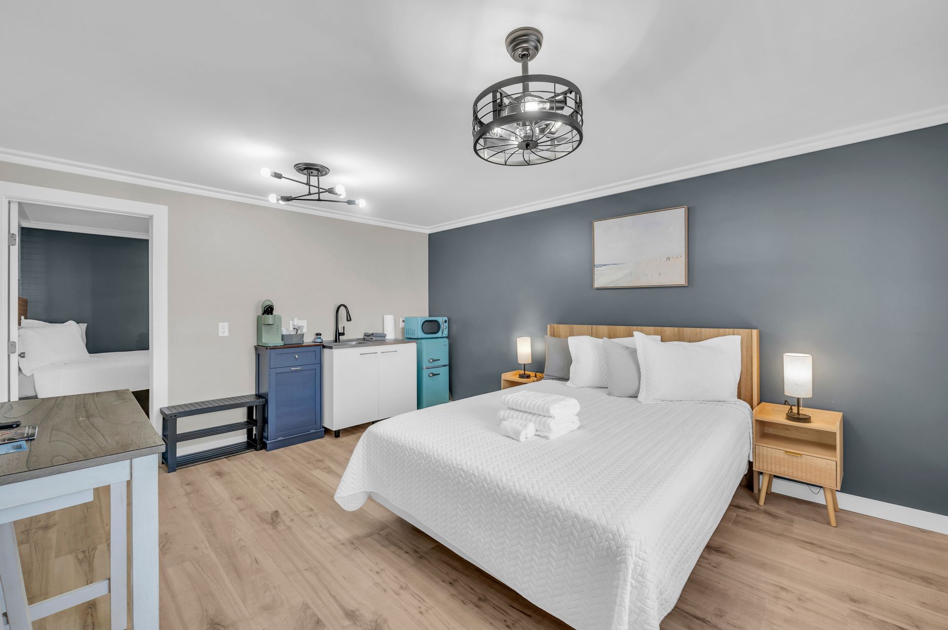 A studio apartment with a bed, kitchenette, and doorway to a second bedroom; blue and gray walls.