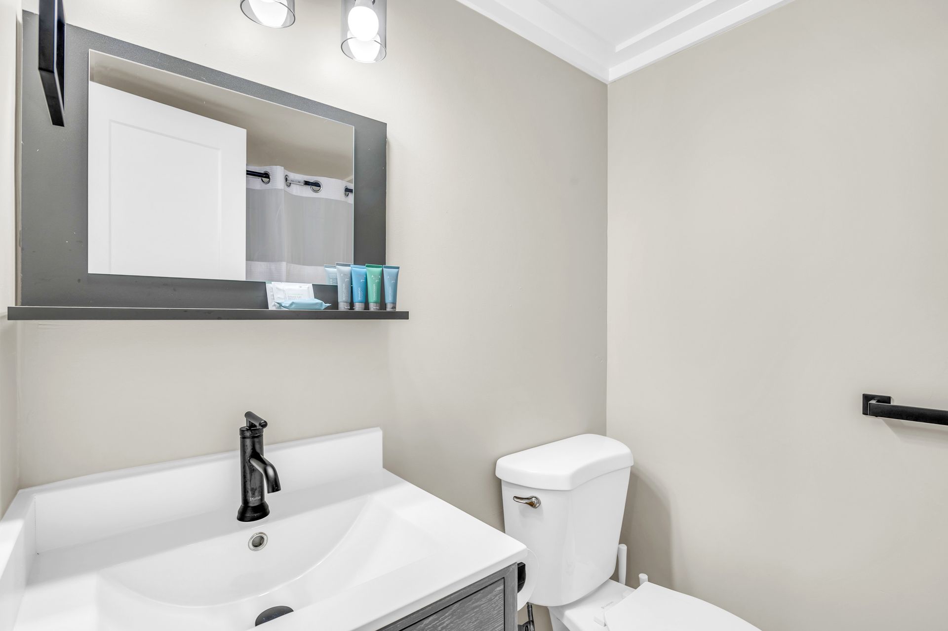 A small bathroom with a white sink, toilet, and gray-framed mirror. The walls are a light beige.