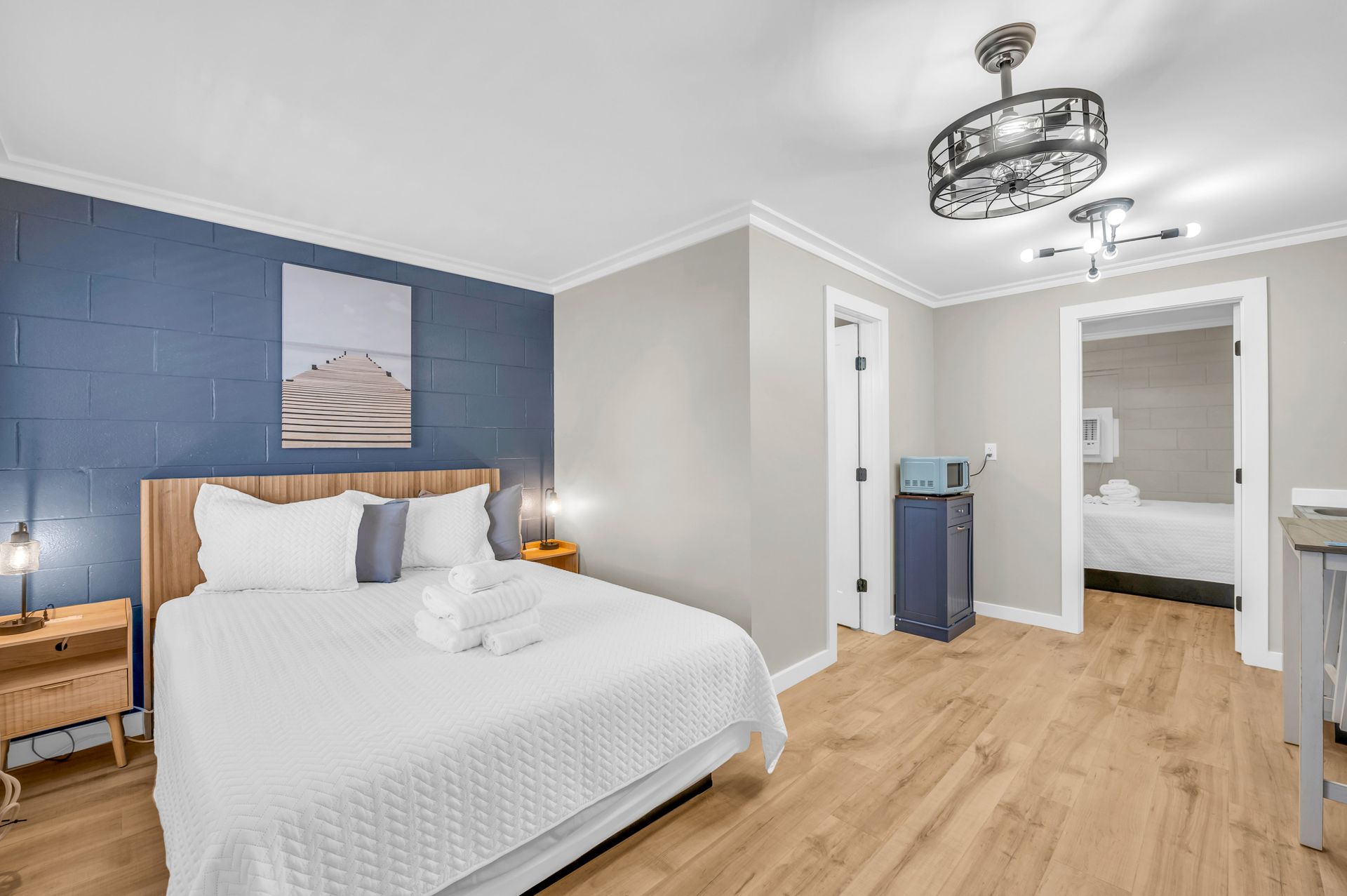 Bedroom with a queen bed, blue accent wall, and doorway to a bathroom. Light wood floors and trim throughout.