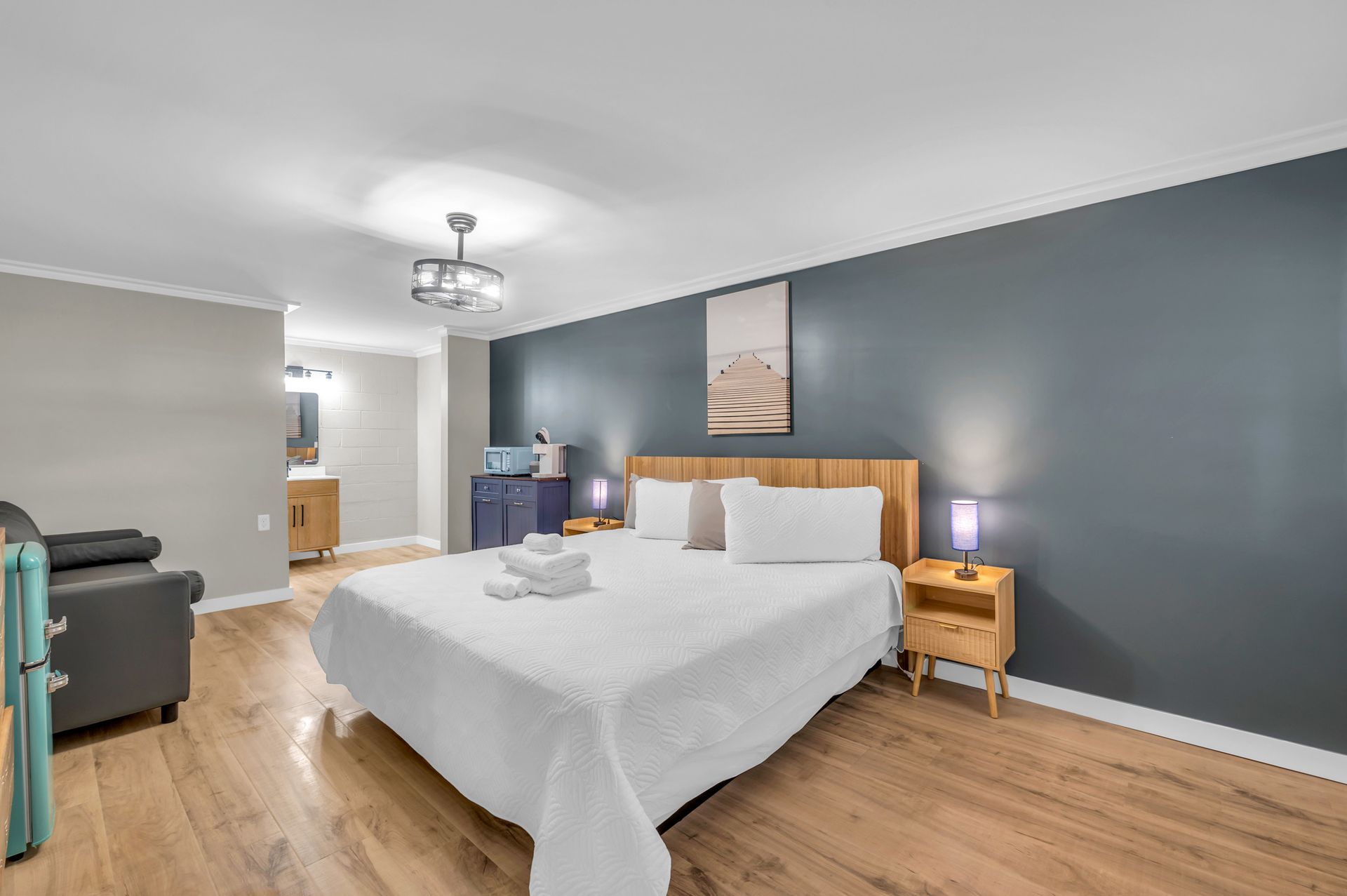 A small, modern hotel room featuring a bed, nightstand, and a seating area, with a blue accent wall.