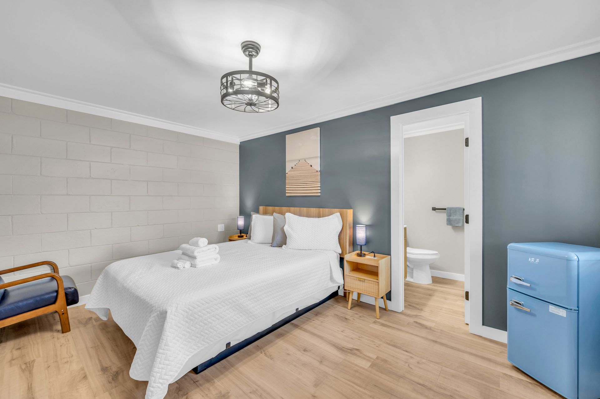 Bedroom with queen bed, blue accent wall, open doorway to bathroom, blue mini-fridge.