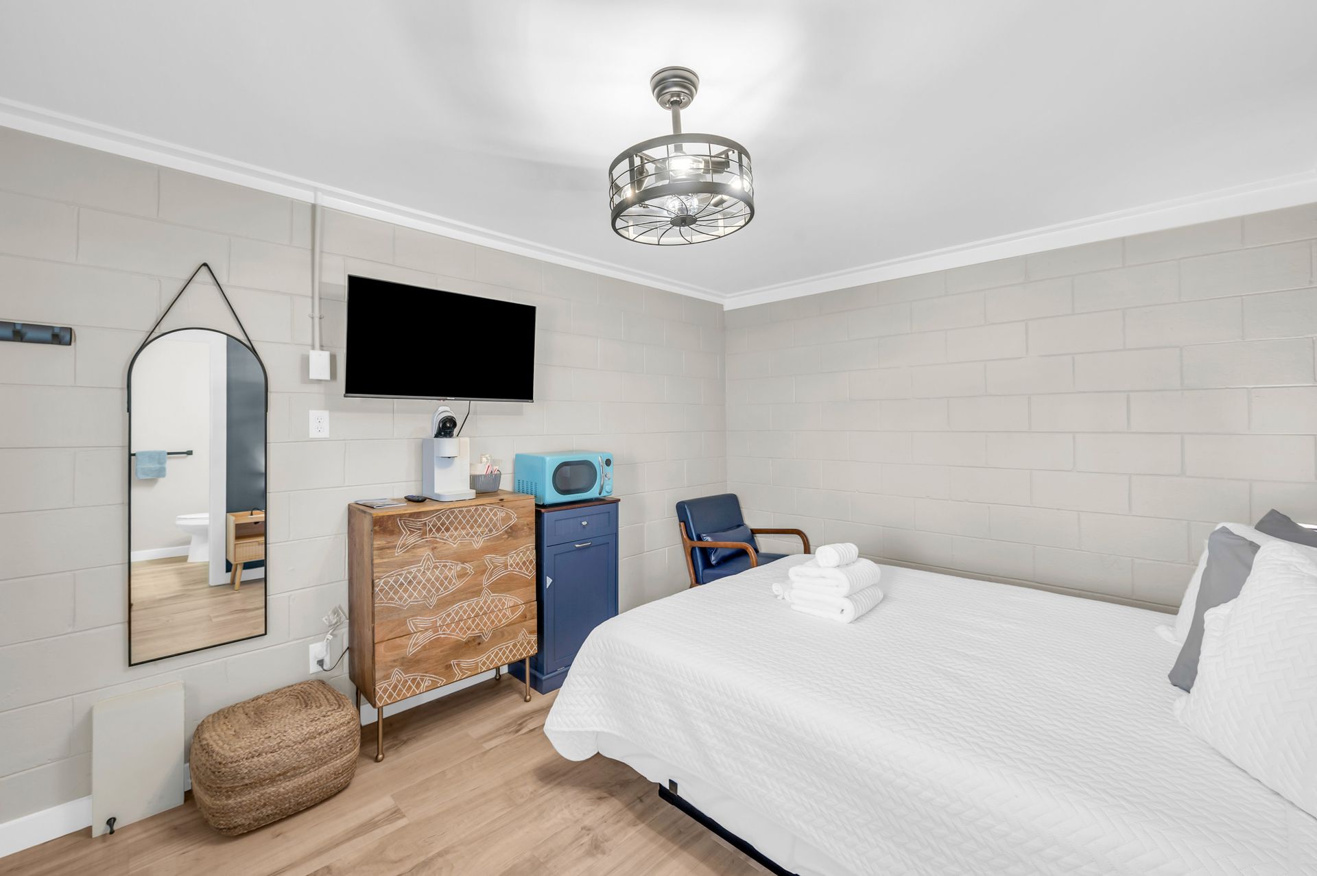 A small bedroom with a bed, dresser, TV, mirror, and blue accents; neutral tones prevail.