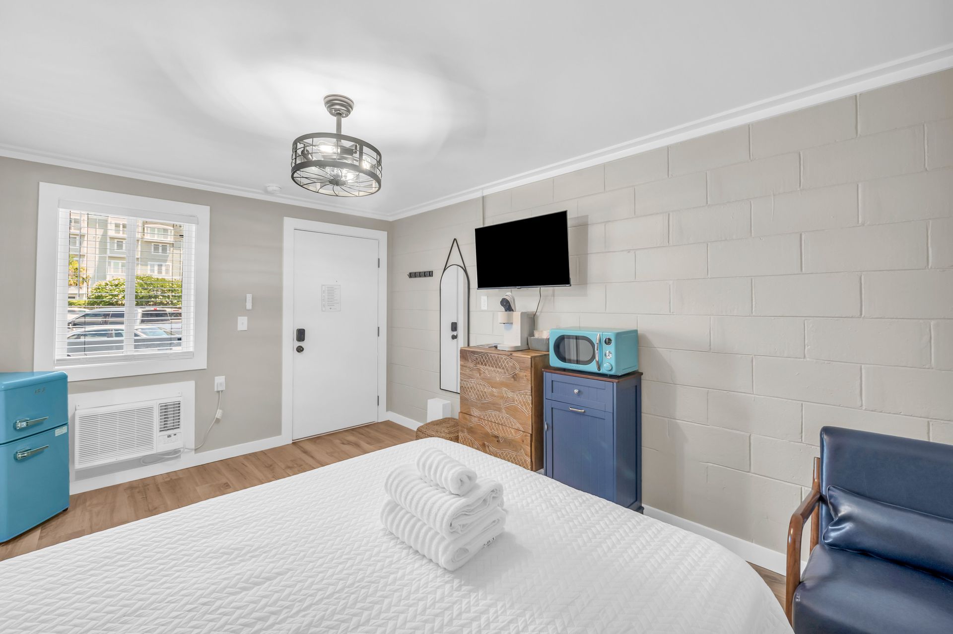 Bedroom with a white bed, a blue mini fridge, and a mounted TV on a grey brick wall.