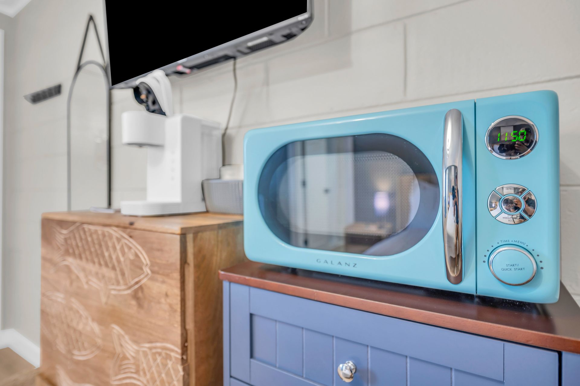 A light blue retro microwave sits on a blue cabinet next to a wooden box, with a coffee maker on top.